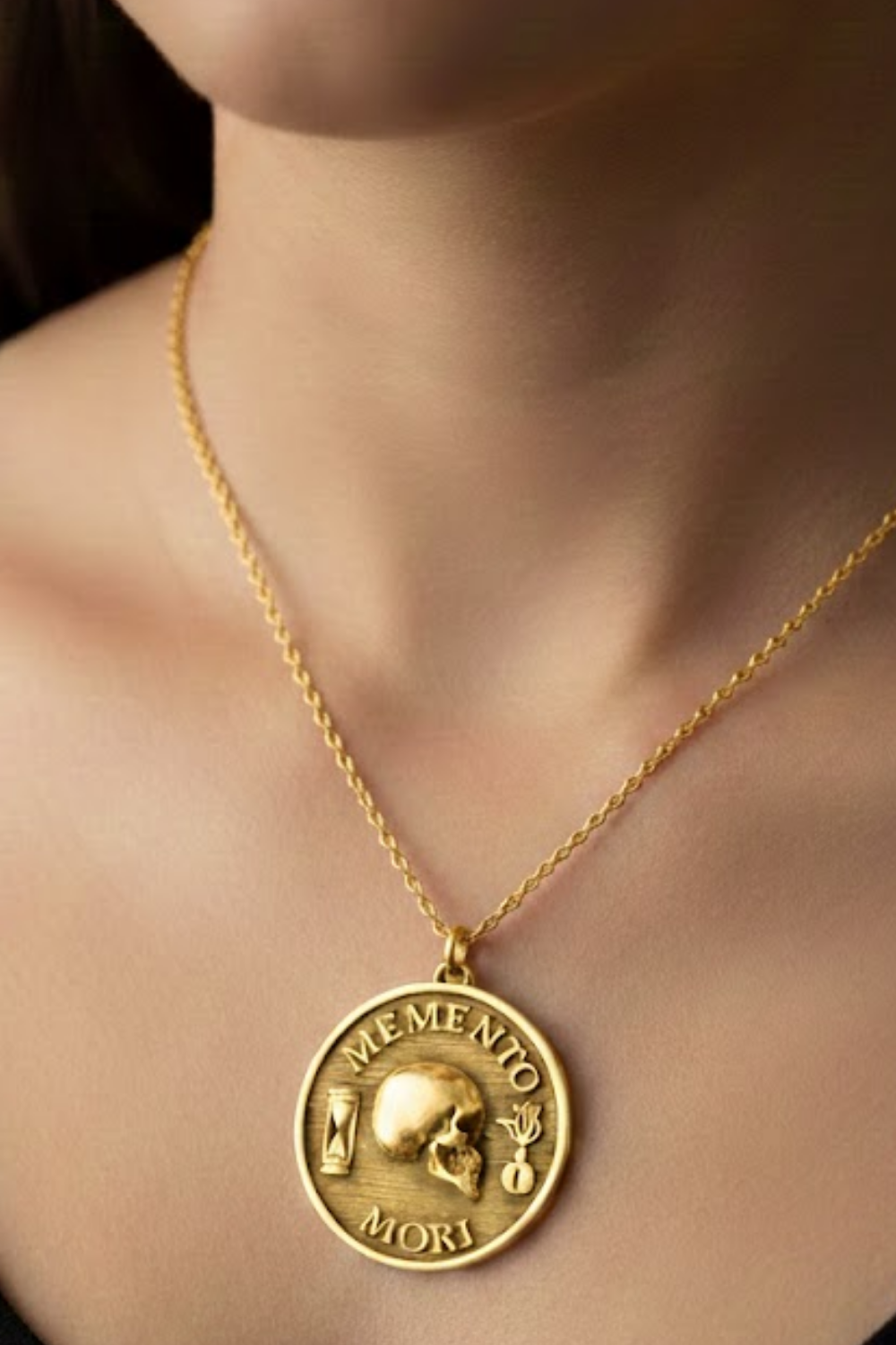 A gold-colored pendant necklace with a circular medallion featuring a skull and the Latin phrase "Memento mori" (which means "life after death").