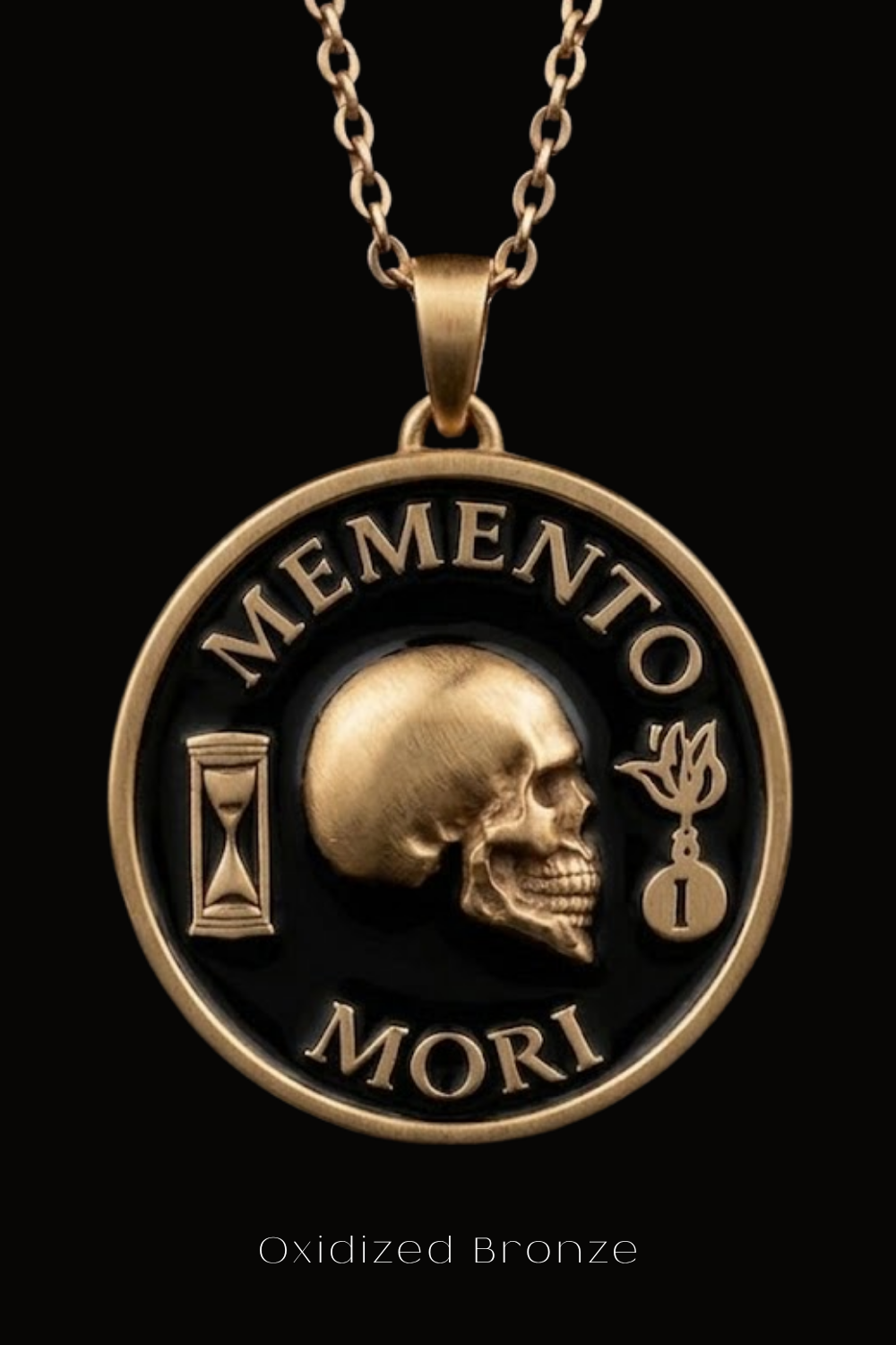 a gold-colored pendant with a black background and a gold-colored skull design. The pendant has the words "MEMENTO MORI" inscribed on it, which translates to "Memento mori" in English.