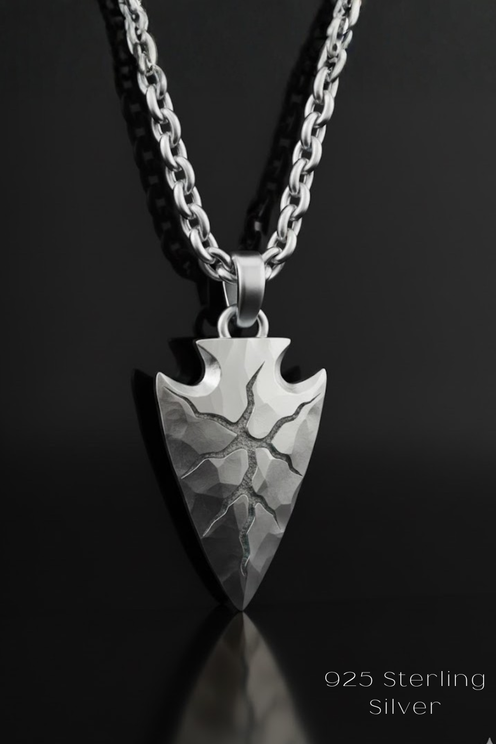 A silver pendant necklace with a pointed arrow-shaped pendant featuring a cracked design.
