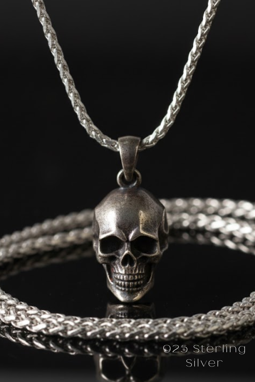 A silver-toned pendant necklace with a skull pendant is displayed against a dark background.