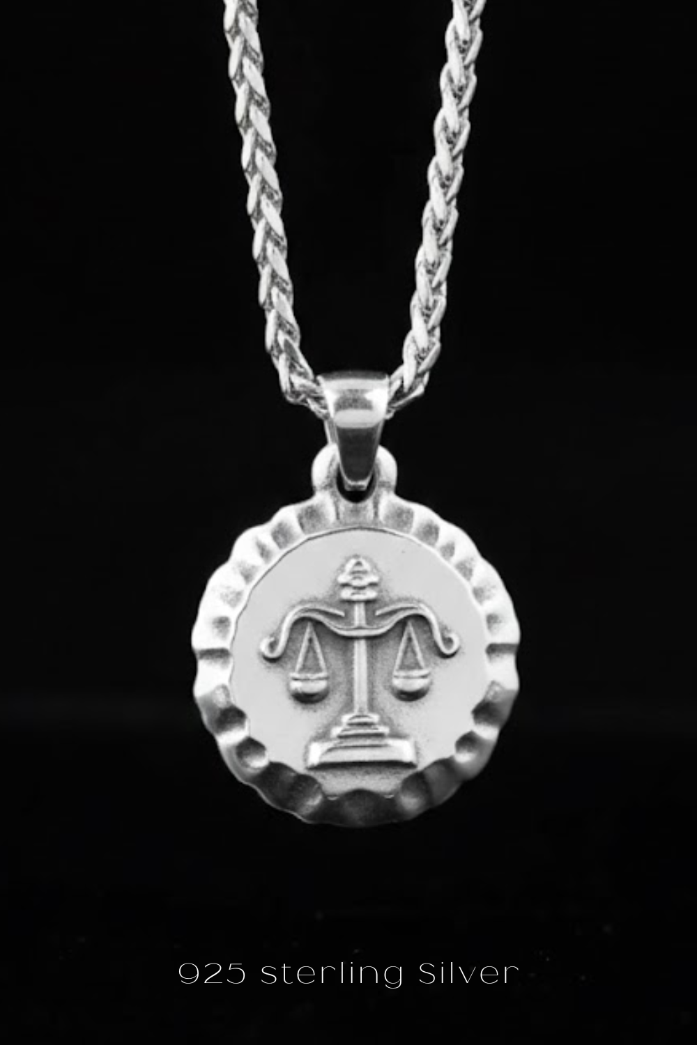 A silver-colored pendant necklace with a circular medallion featuring a scale of justice symbol.