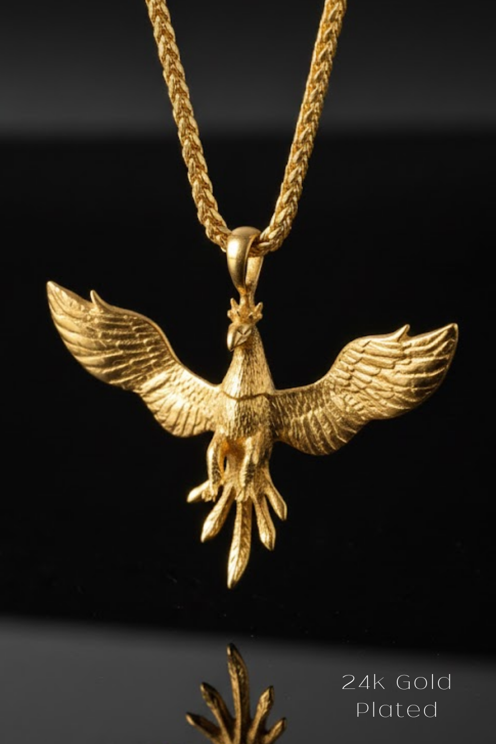 A gold-plated pendant in the shape of a phoenix, with wings spread wide, is displayed against a black background.