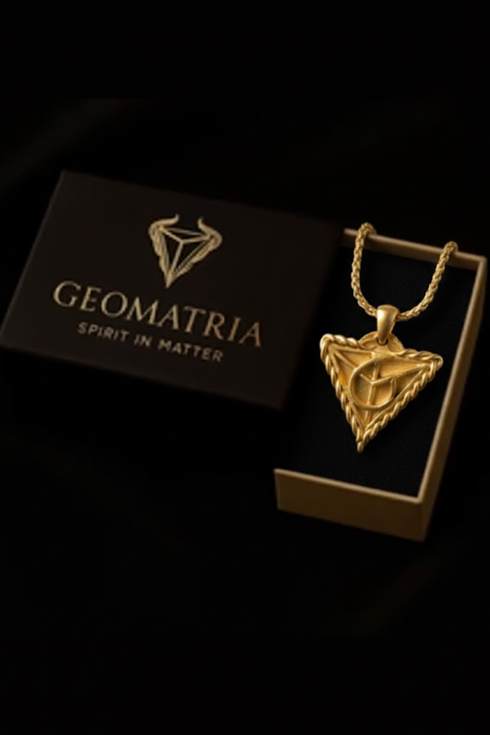 A gold necklace with a pendant is displayed in a black box with the text "Geomatria" and "SPIRIT IN MATTERS" printed on it.