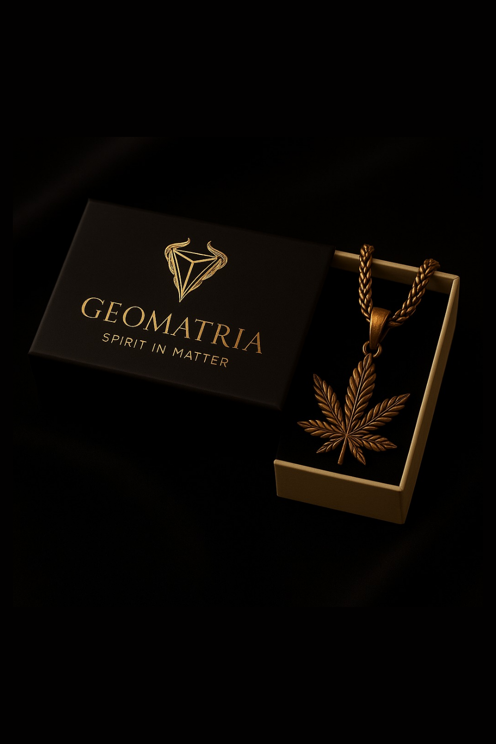 a gold pendant with a leaf design, placed inside a black box with the word "Geomatria" printed on it.