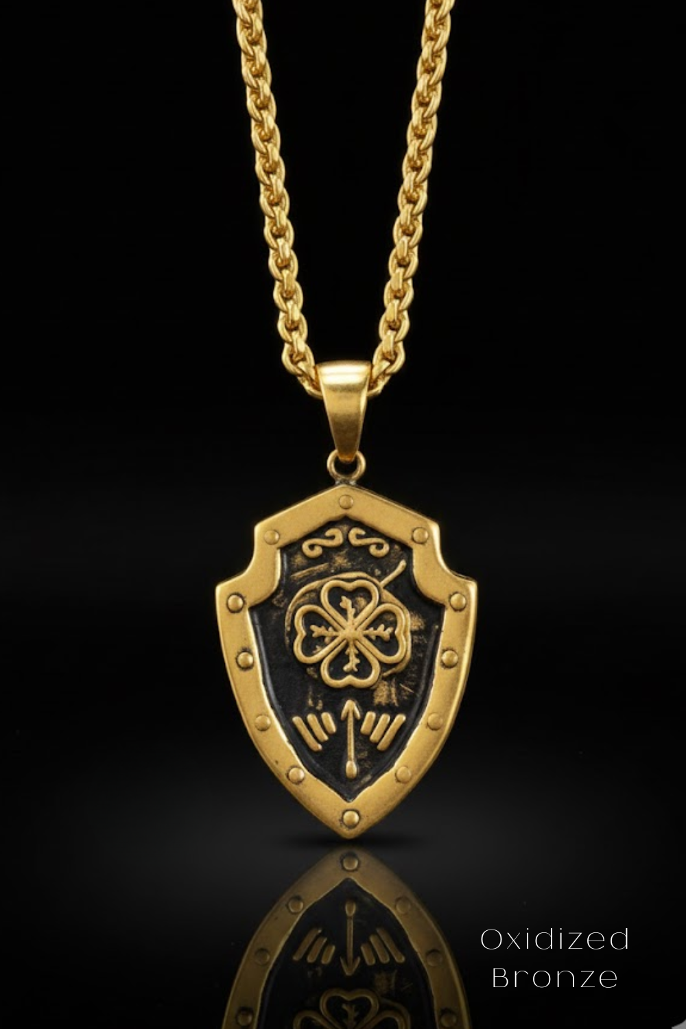 A gold-colored pendant necklace with a shield-shaped pendant featuring a four-leaf clover design and decorative elements.