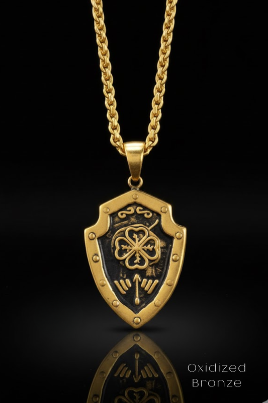 A gold-colored pendant necklace with a shield-shaped pendant featuring a four-leaf clover design and decorative elements.