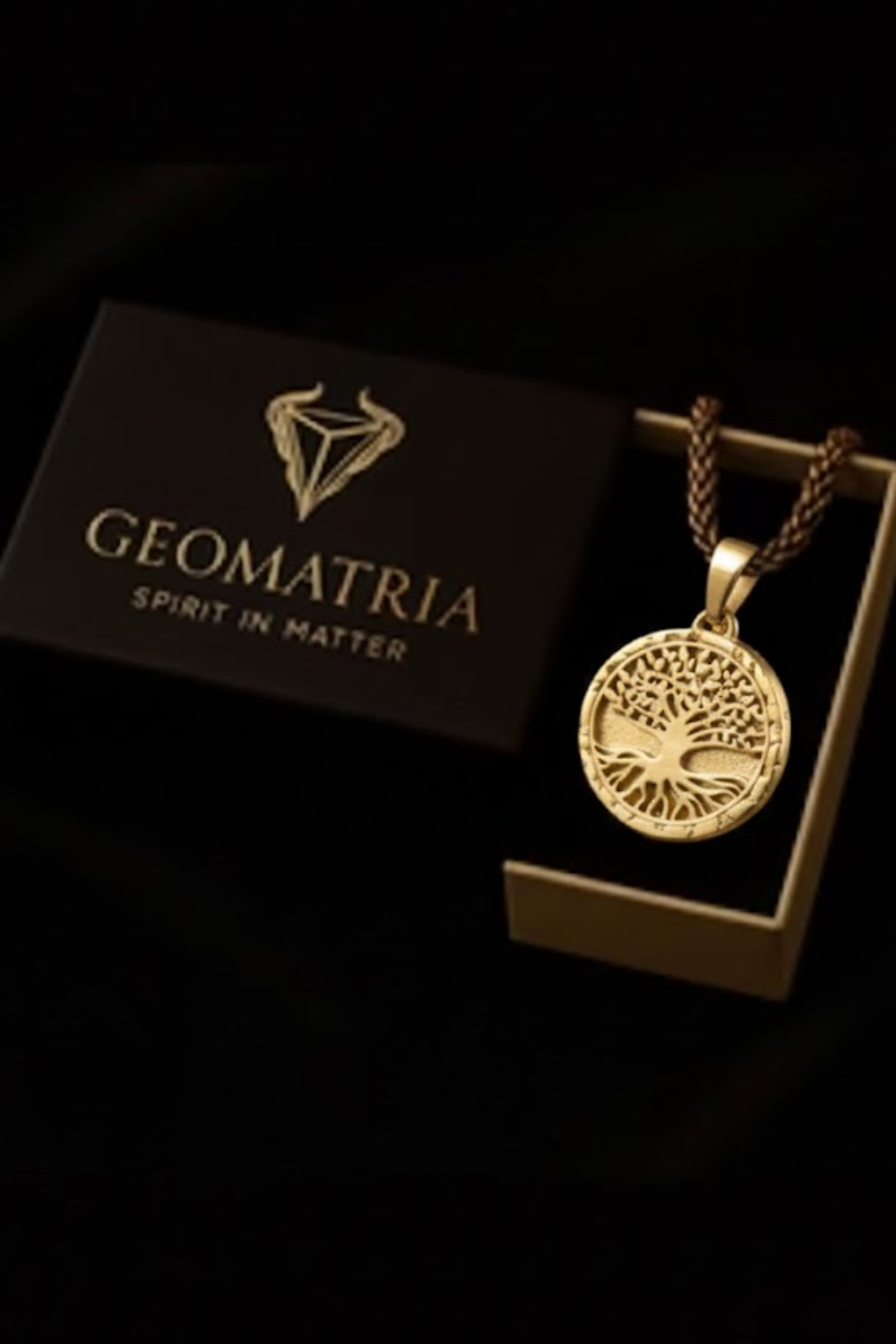 A gold-colored pendant necklace with a tree design, displayed in a black box with the Geomatria logo.
