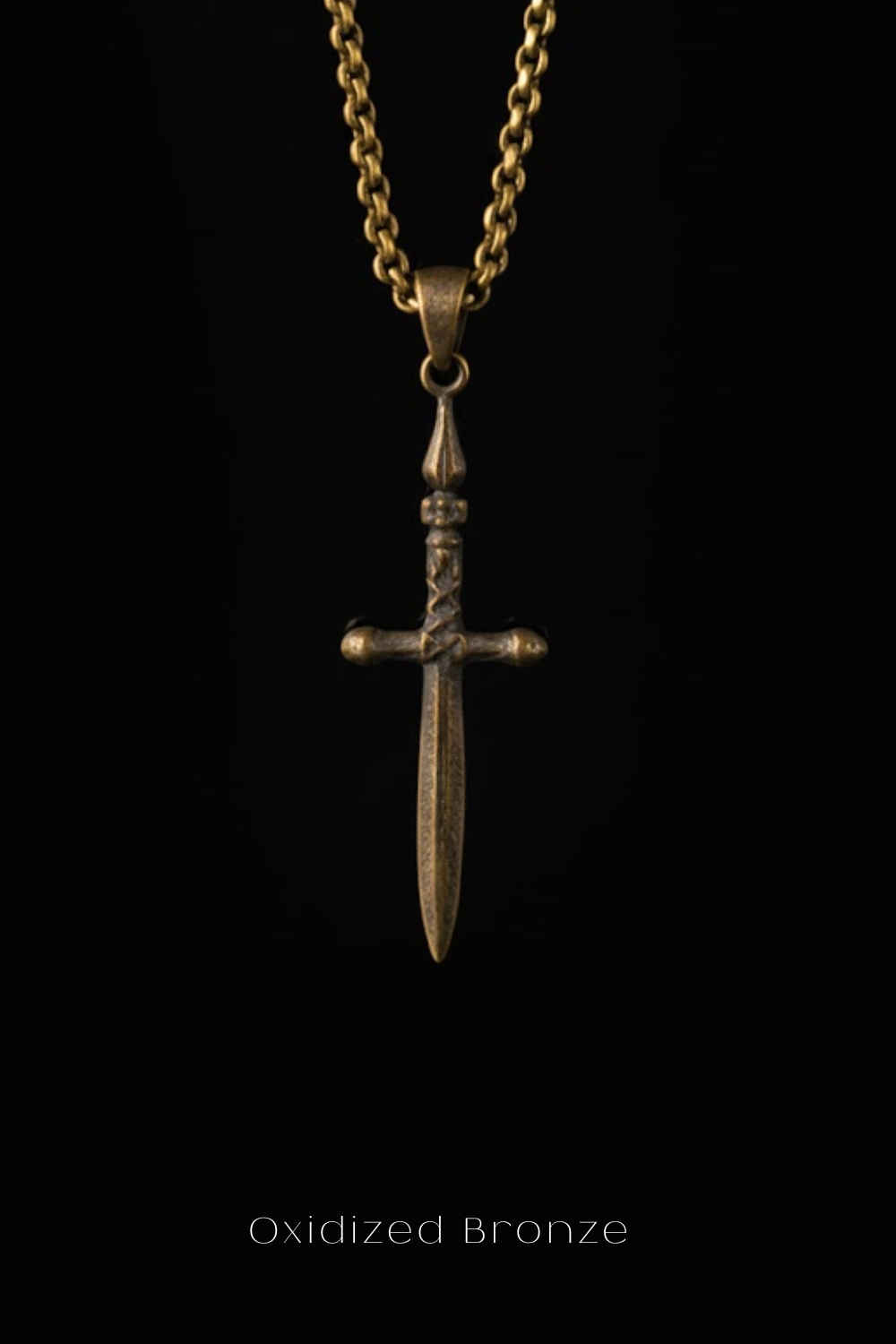 A close-up view of a bronze cross pendant hanging from a chain against a black background.