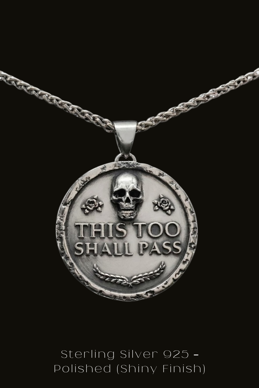 A silver pendant necklace with a circular medallion featuring a skull and the text "THIS TOO SHALL PASS" in a bold, metallic font.