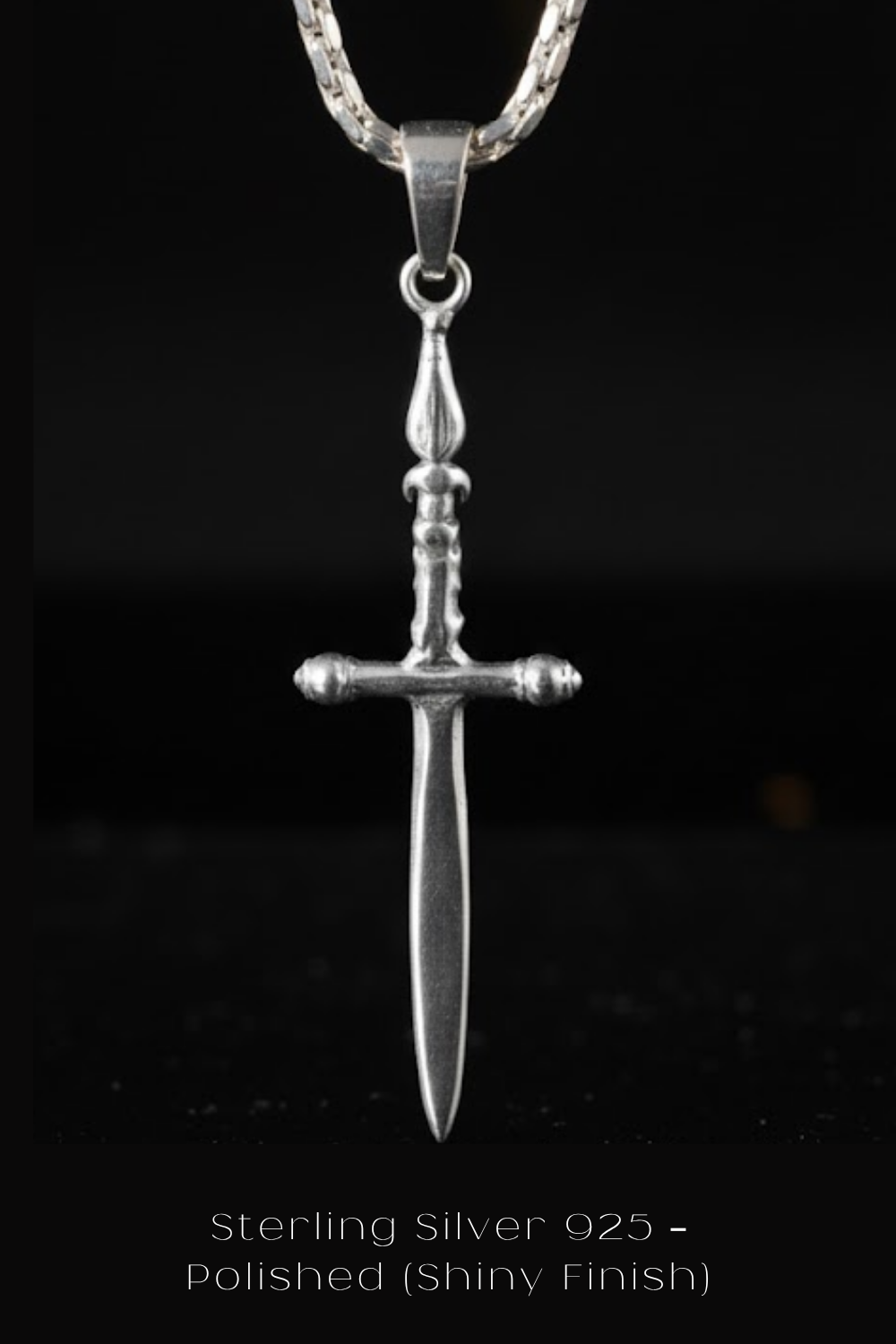 A silver-colored pendant in the shape of a sword, suspended from a chain against a black background.