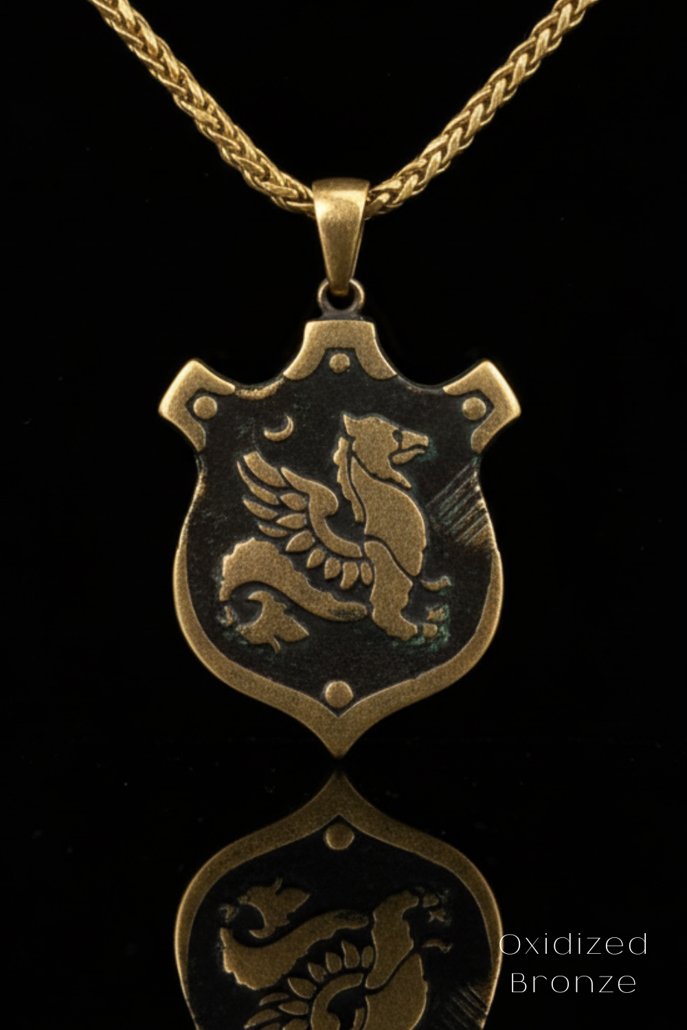 A gold-colored pendant necklace with a shield-shaped pendant featuring a winged creature, possibly a dragon or a mythical bird.