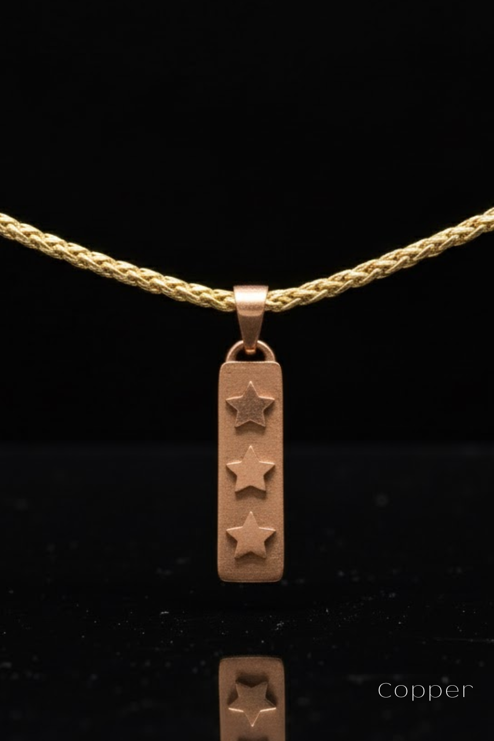 A copper-colored pendant with three stars is suspended from a gold-colored chain against a black background.