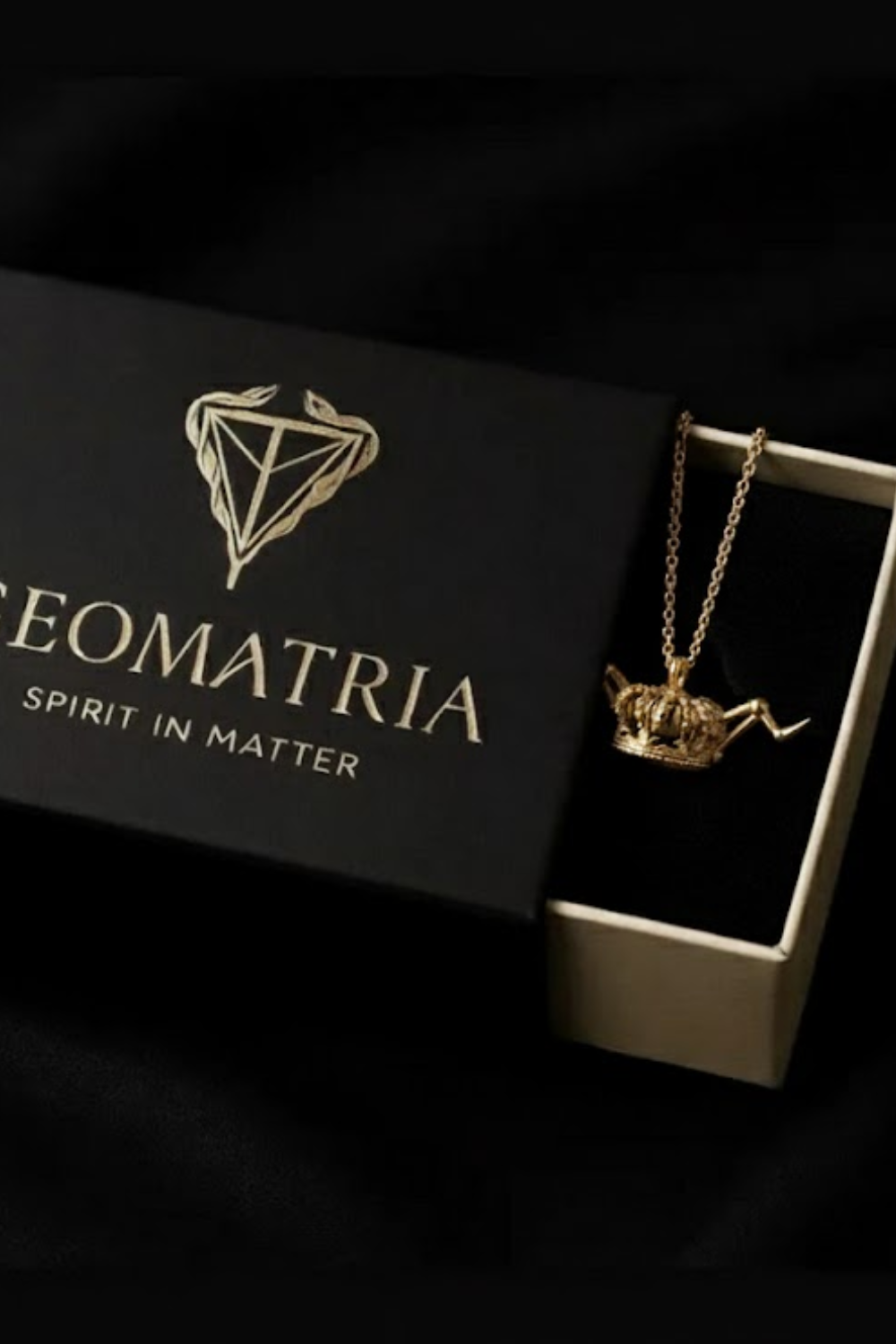 A gold crown pendant is displayed in a black box with the text "Geomatria" and "SPIRIT IN MATTERS" printed on it.