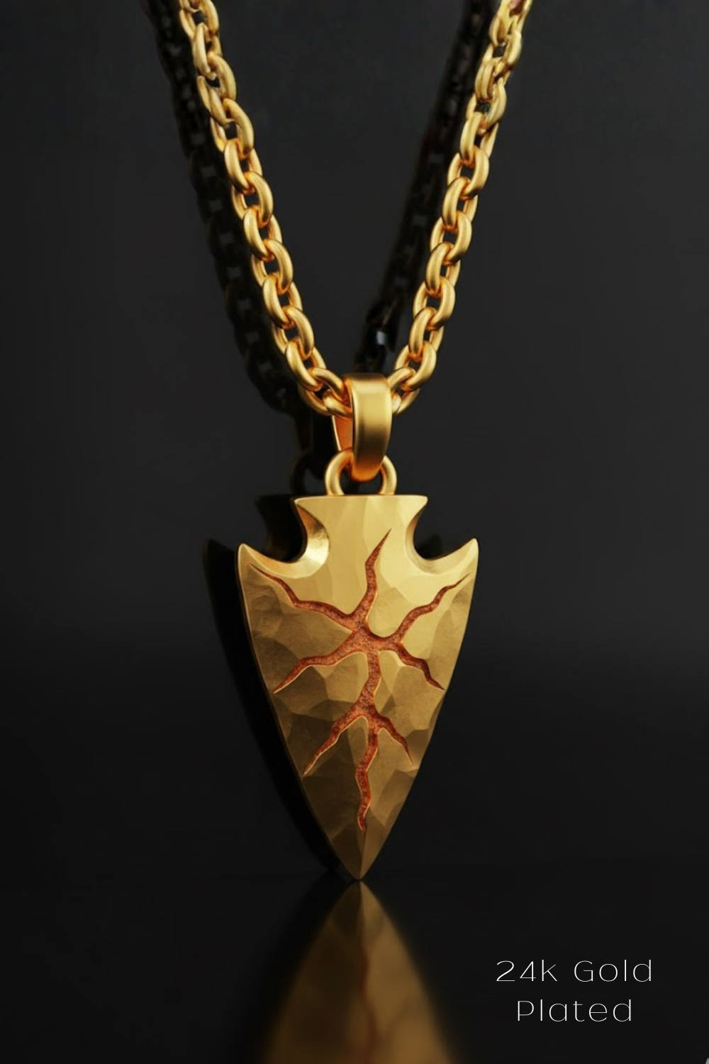 A gold-plated pendant featuring a pointed arrow design with a cracked pattern, suspended from a chain against a black background.