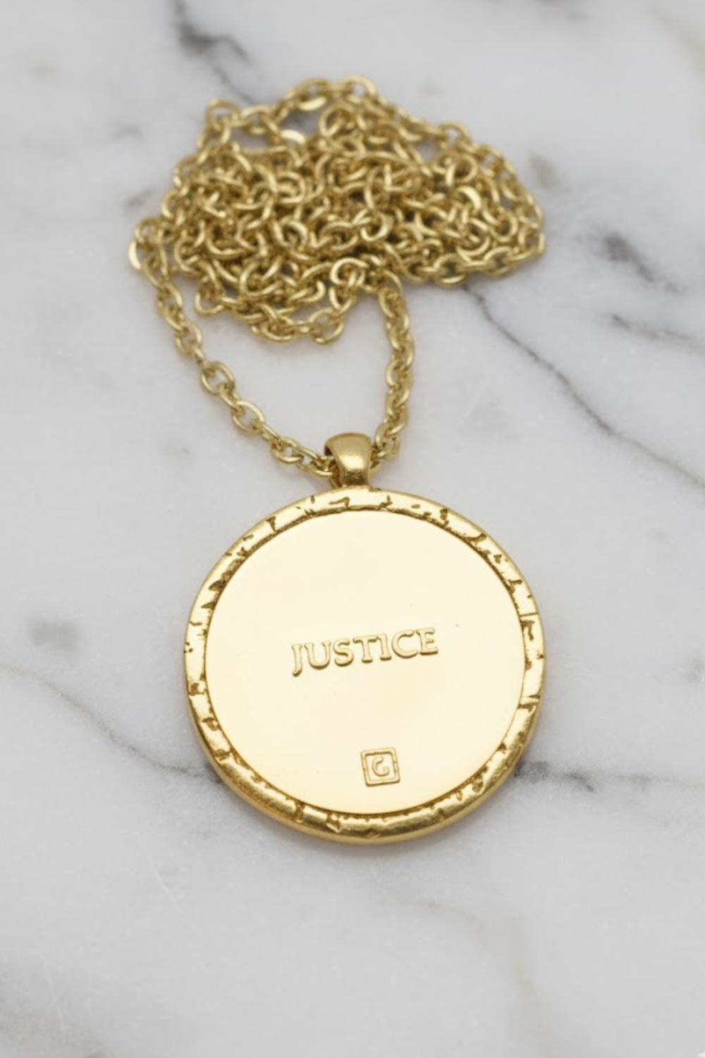 A gold-colored necklace with a round pendant featuring the word "JUSTICE" engraved on it.