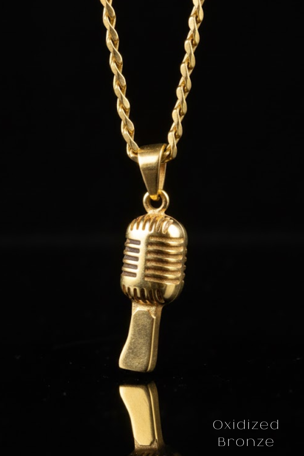 A gold-colored microphone pendant is suspended from a chain against a black background.