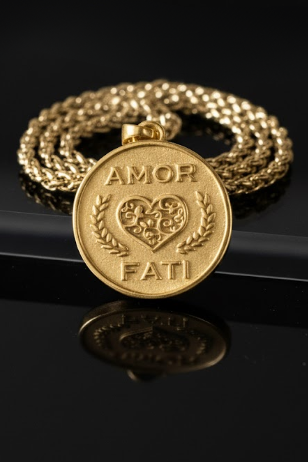 A gold-colored pendant with the words "Amor Fati" engraved on it, surrounded by a chain.