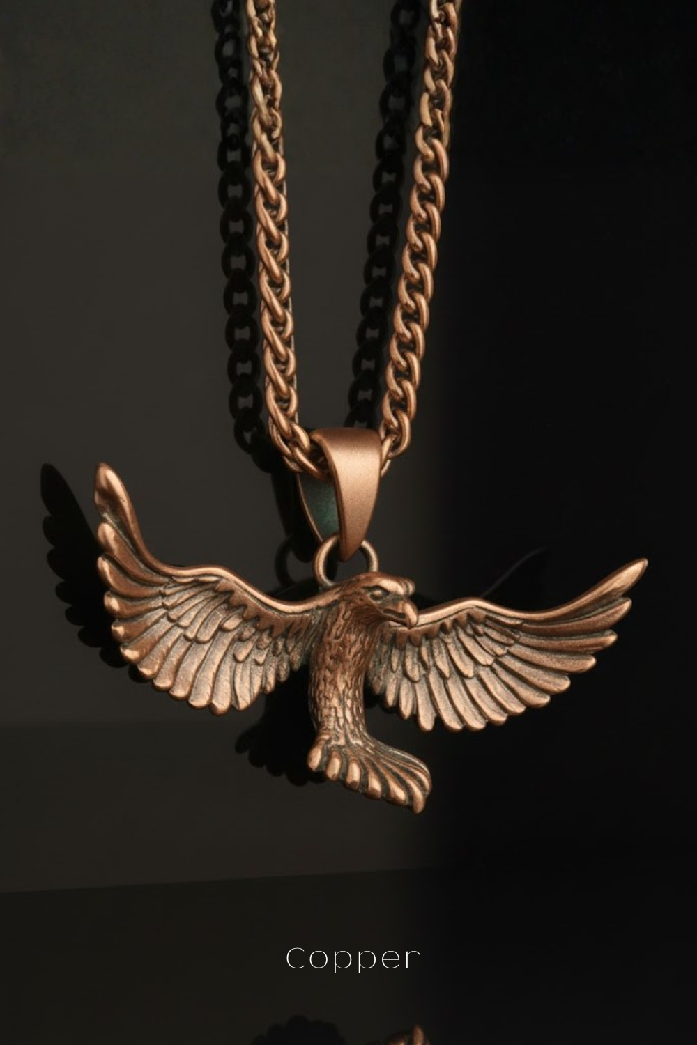 A copper-colored pendant in the shape of a bird with outstretched wings, suspended from a chain.