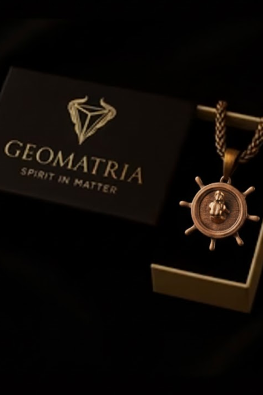 a pendant with a ship's wheel design, placed inside a box with a dark background.