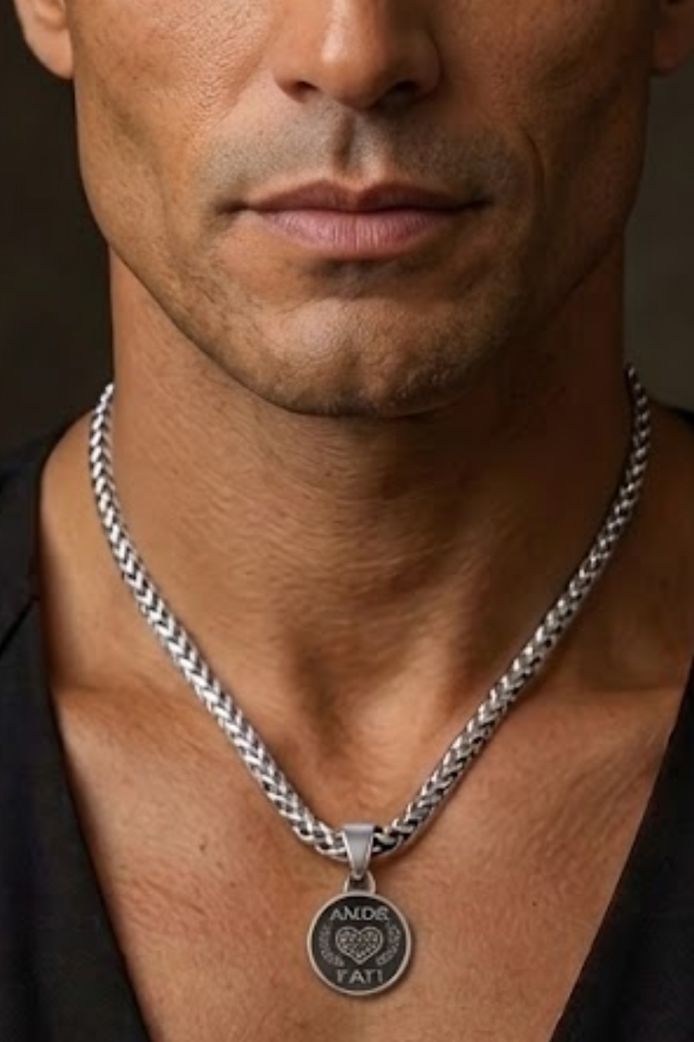 A close-up of a man's neck and chest area, with a silver chain necklace and a pendant featuring a heart-shaped design.