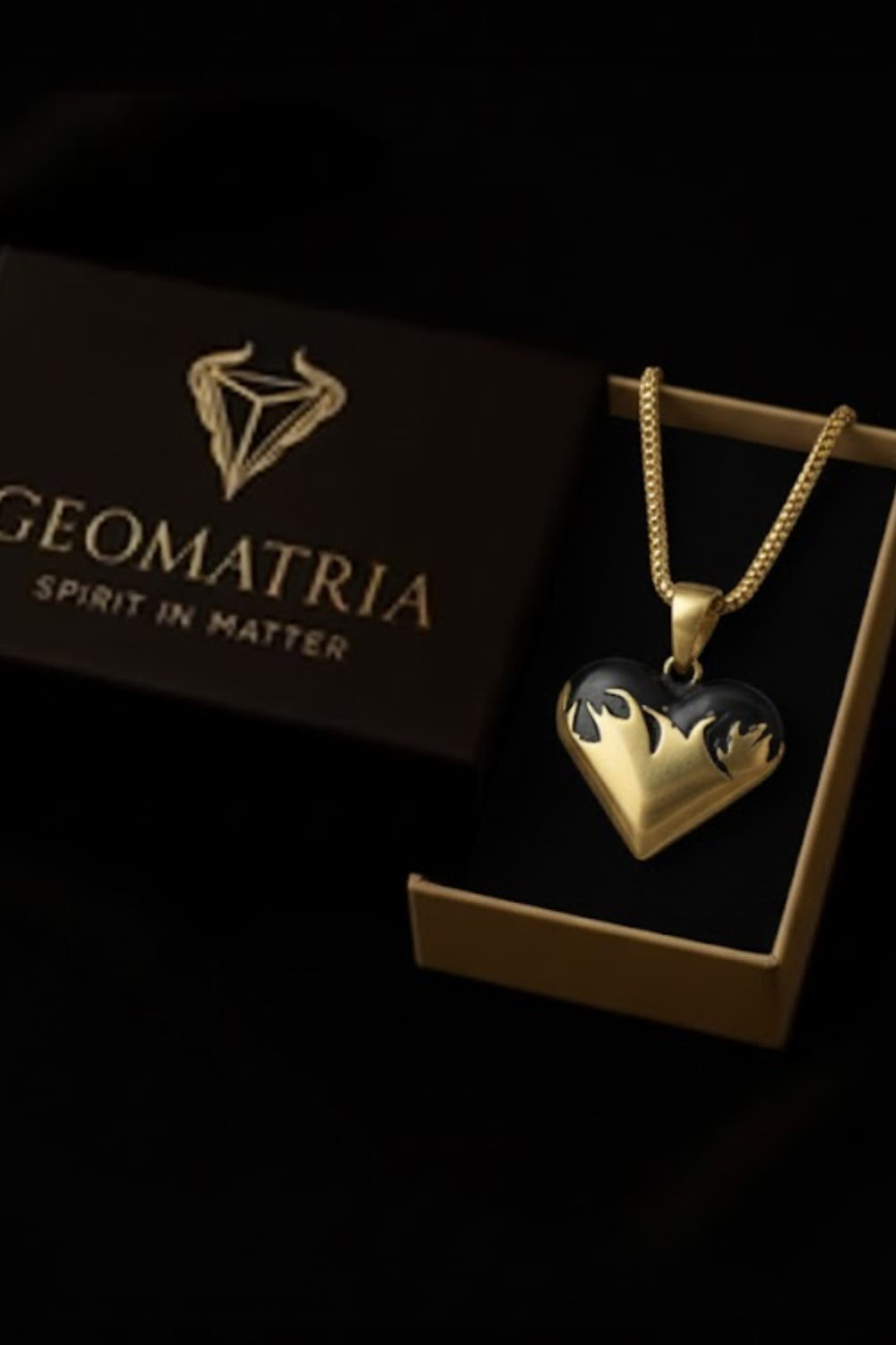 A gold heart-shaped pendant with flames on it, displayed in a gold box with the Geomatria logo.