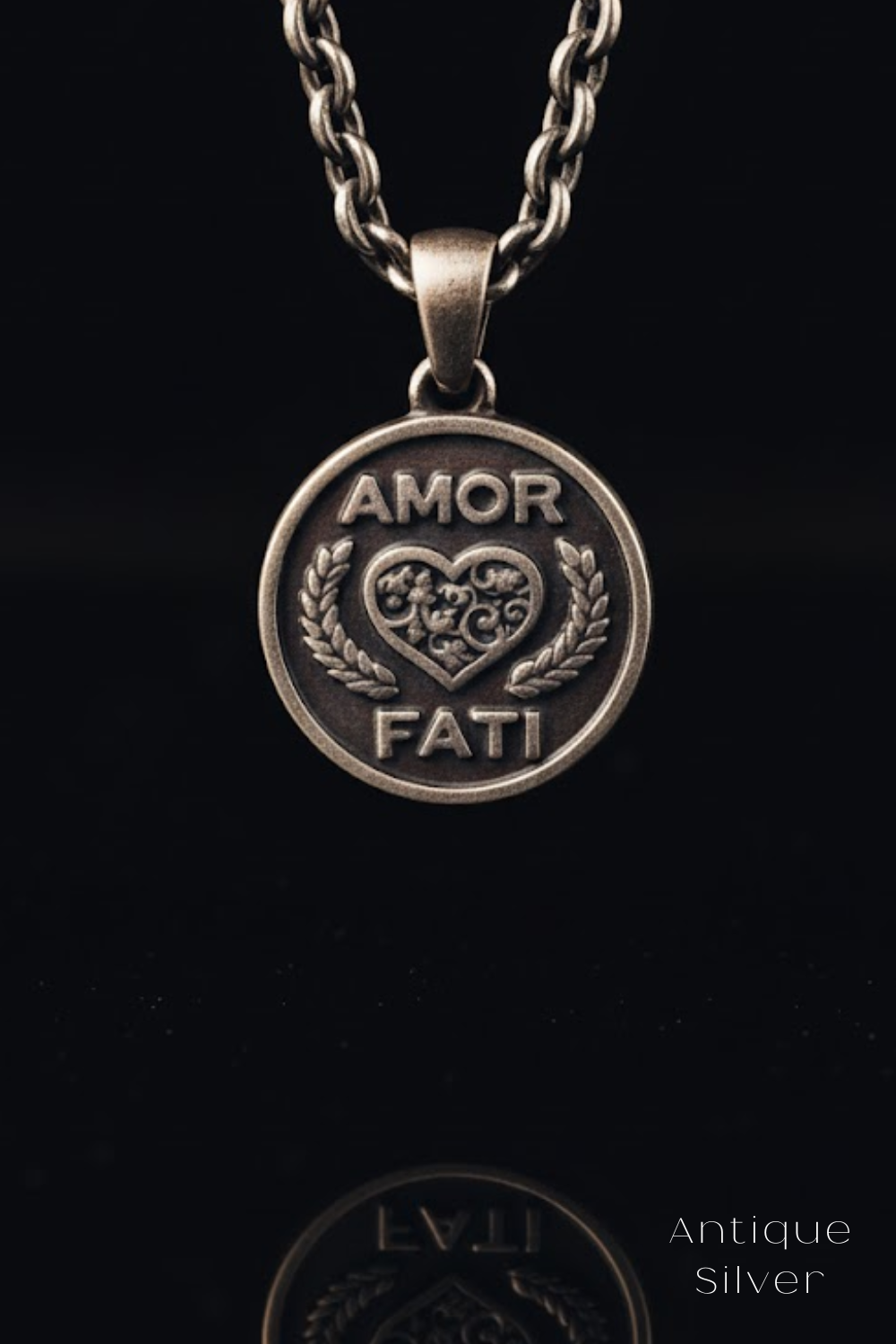 A silver pendant with the words "Amor Fati" engraved on it, which means "love is a feast" in Italian. The pendant is suspended from a chain against a black background.