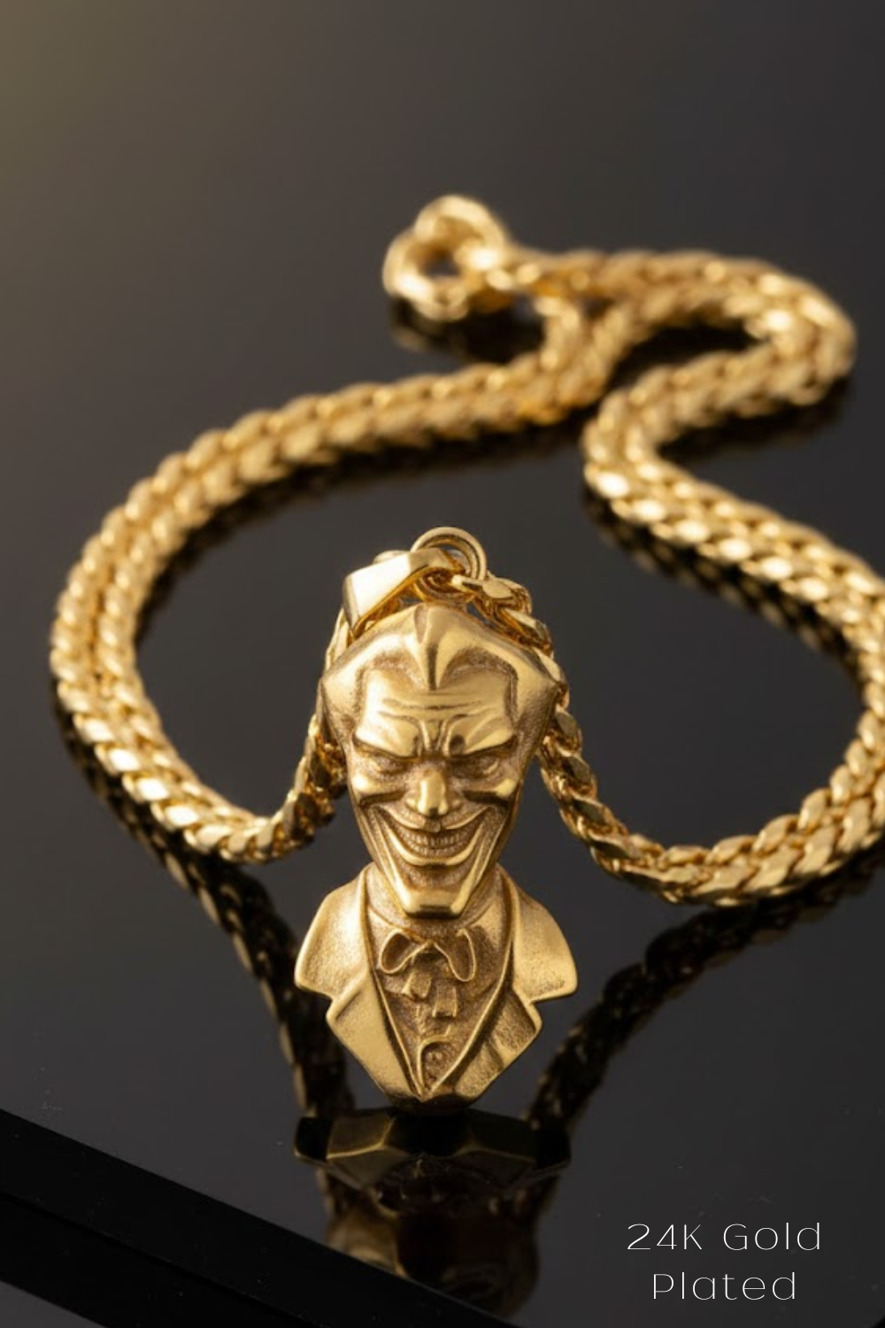 A gold-colored pendant in the shape of a smiling man's head, with a chain around it, is displayed on a reflective surface.