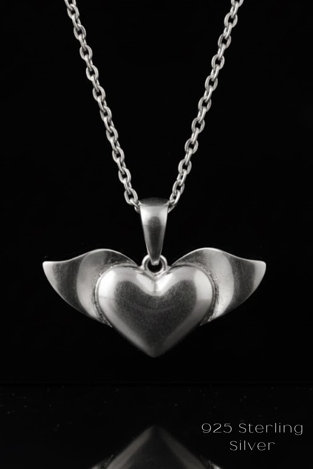 A silver heart-shaped pendant with wings attached, suspended from a chain against a black background.