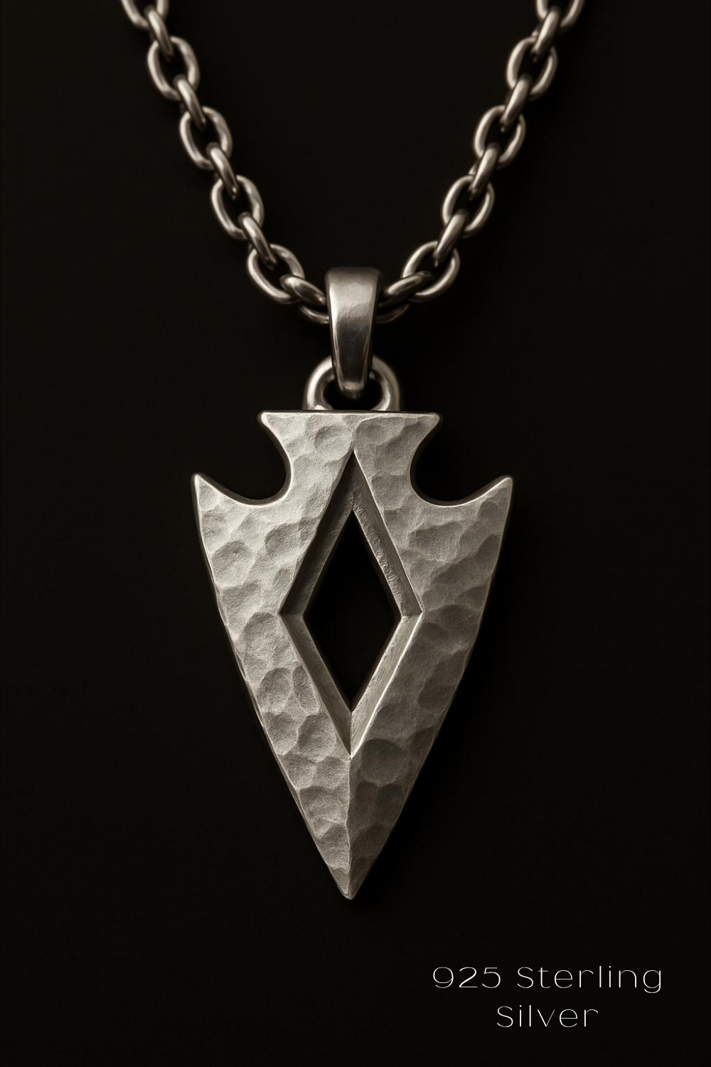 A silver-colored pendant with a diamond-shaped cutout in the center, hanging from a chain against a black background.