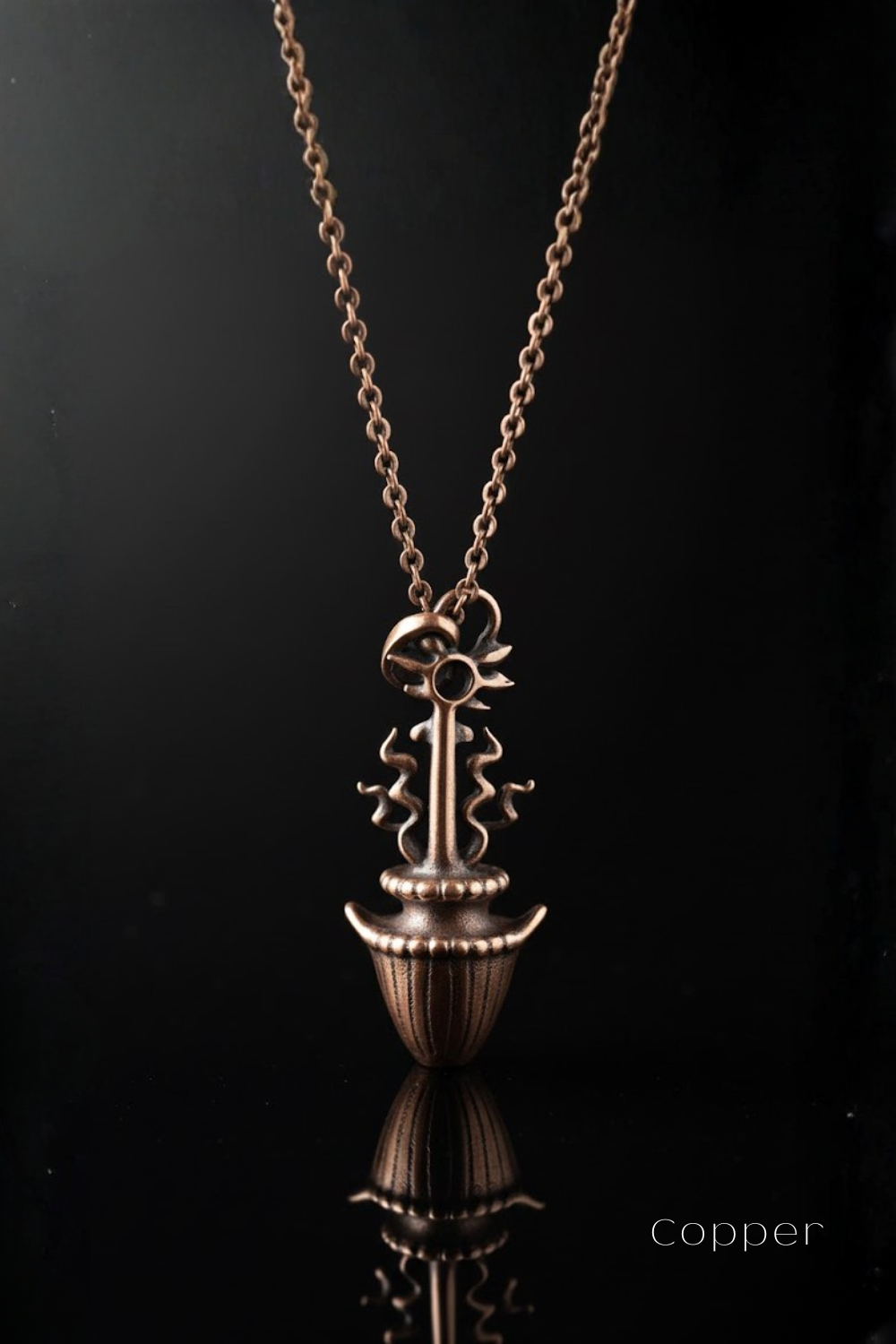 A copper-colored pendant necklace with a decorative design, displayed against a black background.