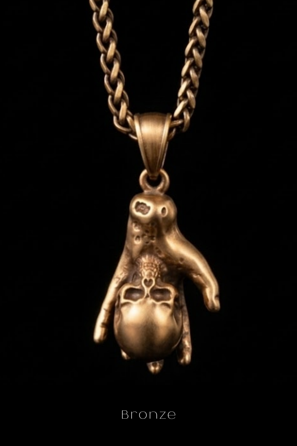A bronze pendant in the shape of a hand holding a skull, suspended from a chain.