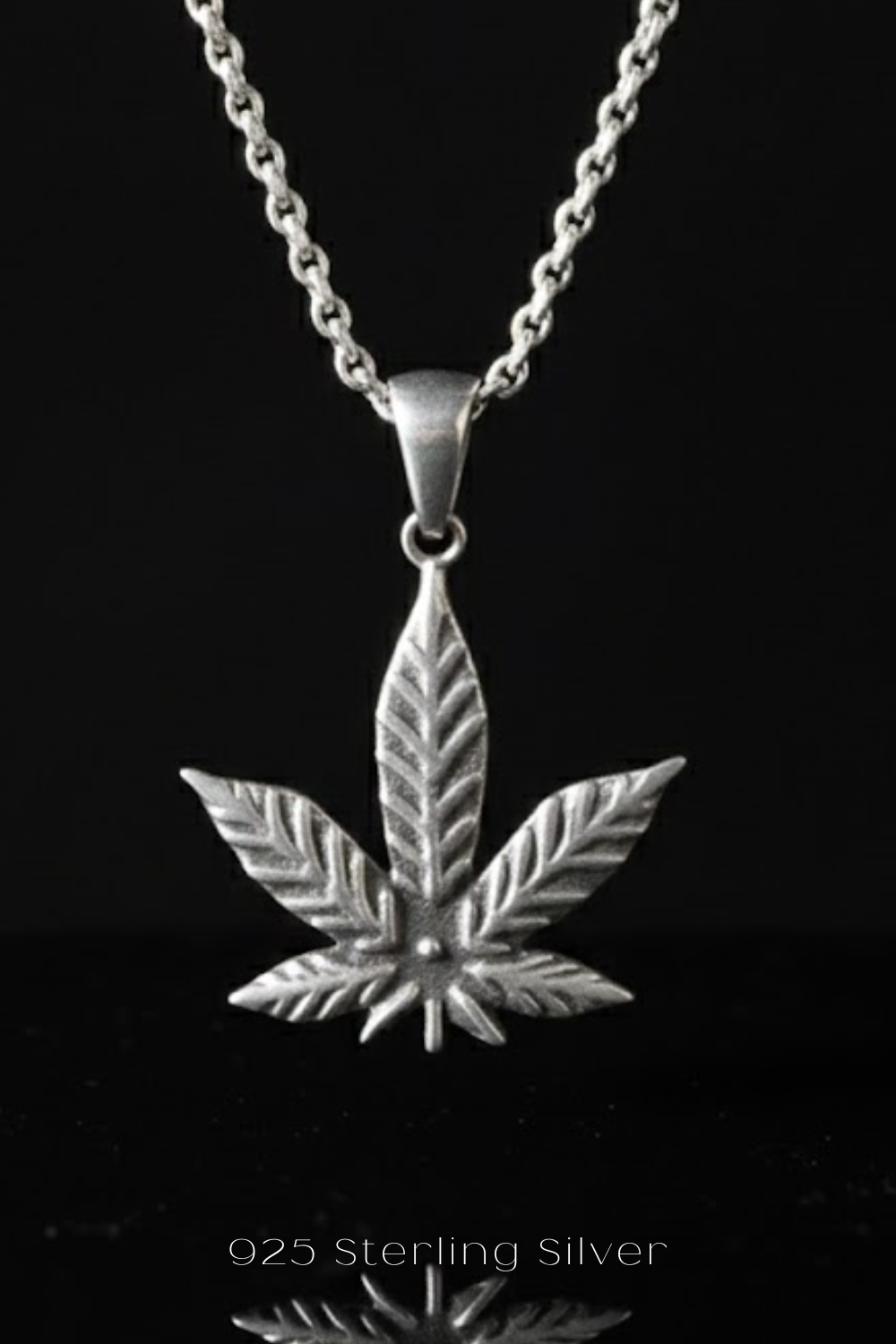 A silver pendant necklace with a leaf-shaped design, against a black background.