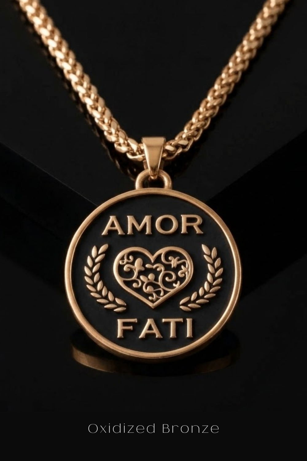 a close-up view of a gold-colored pendant necklace with a circular pendant that displays the text "Amor Fati" in a decorative font.